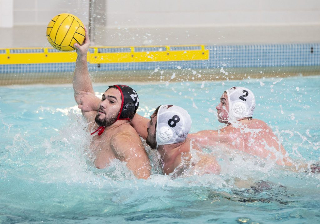Oct 14, 2018; Baltimore, MD, USA; Monmouth Fighting Scots center Jesus Aguirre (21) fires a shot as Austin College 'Roos center Alex Rodriguez (8) and attacker Andrew Pope (2) apply pressure at the Newton White Athletic Center Natatorium. Greg Bartram/betterImage