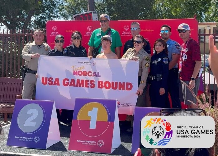 Simon Keenan holds Team NorCal USA Games Bound banner surrounded by supporters and officers after being selected for the 2026 Special Olympics USA Games in Minneapolis.